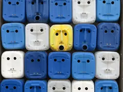 Редици от сини и бели пластмасови туби, чиито дръжки и отвори образуват очи и усти, а една туба е жълта